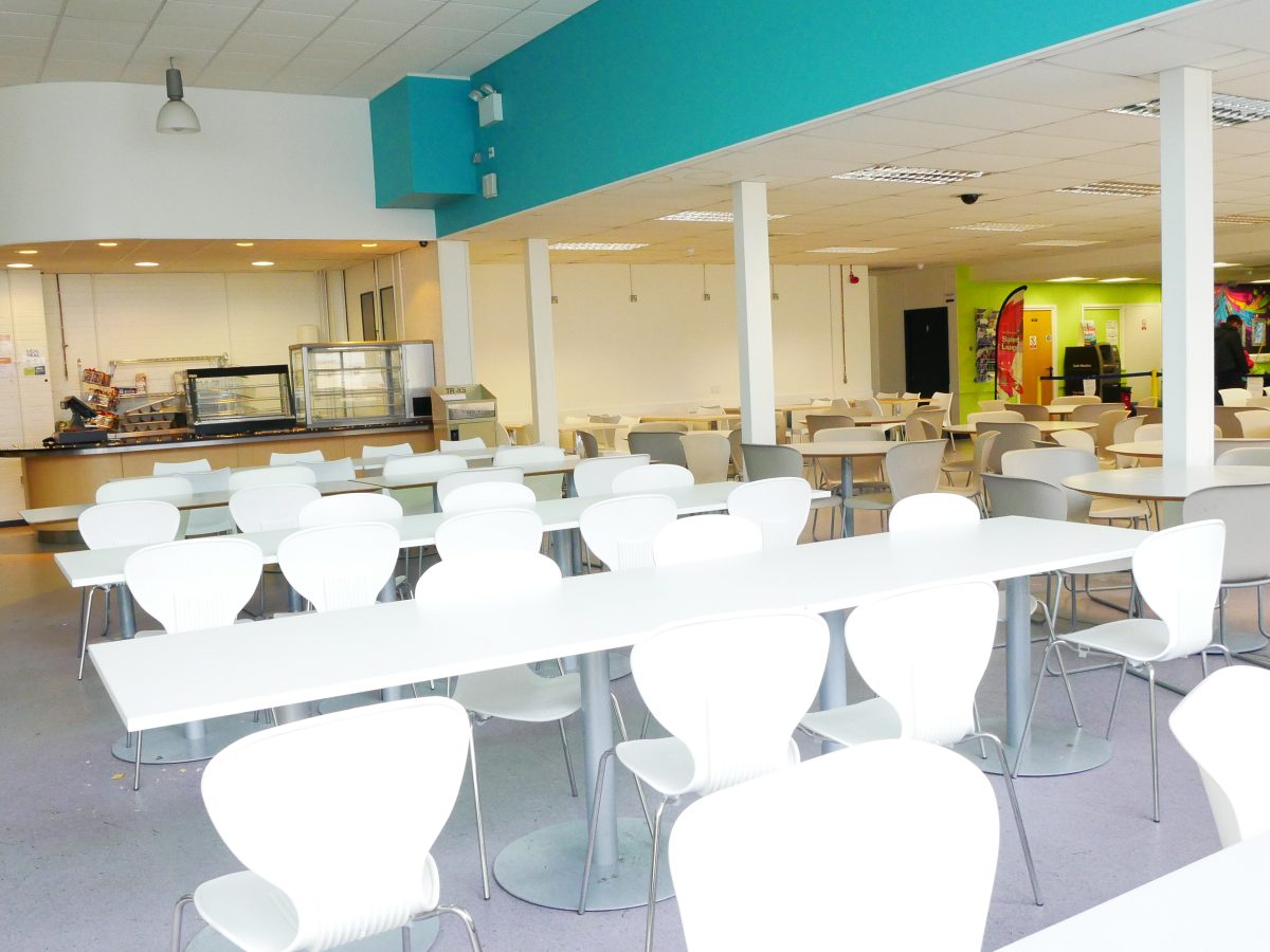 Table and chairs in the Refectory at Rush Green Campus. Food counter in the far back and student lounge far back on the right