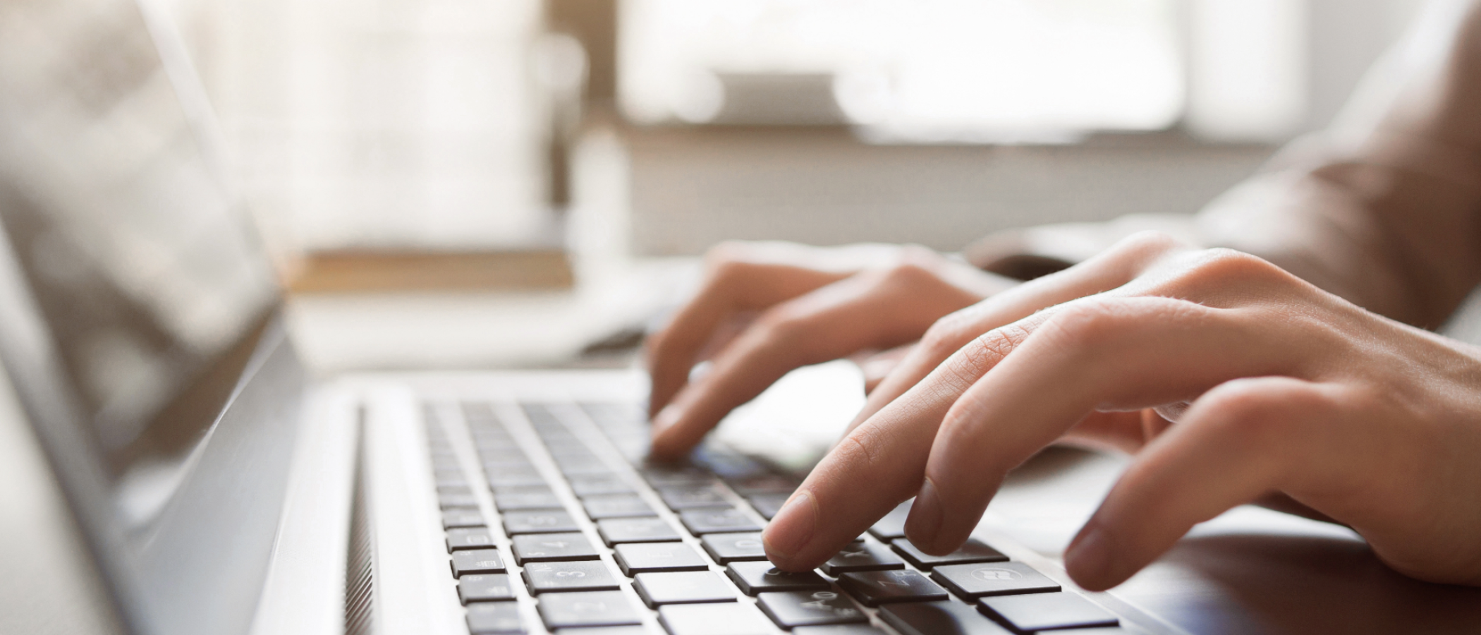 A close-up of hands typing on a laptop keyboard, with the screen and background softly blurred.