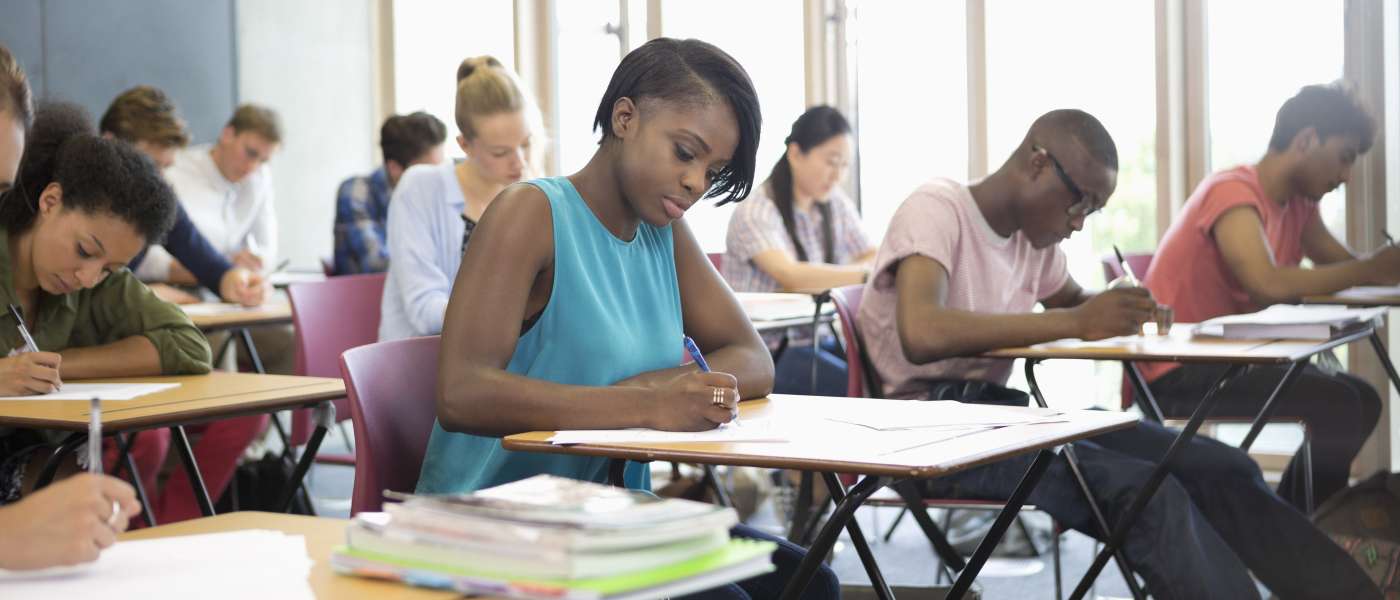 Group of young adult students sat at individual desks taking exams