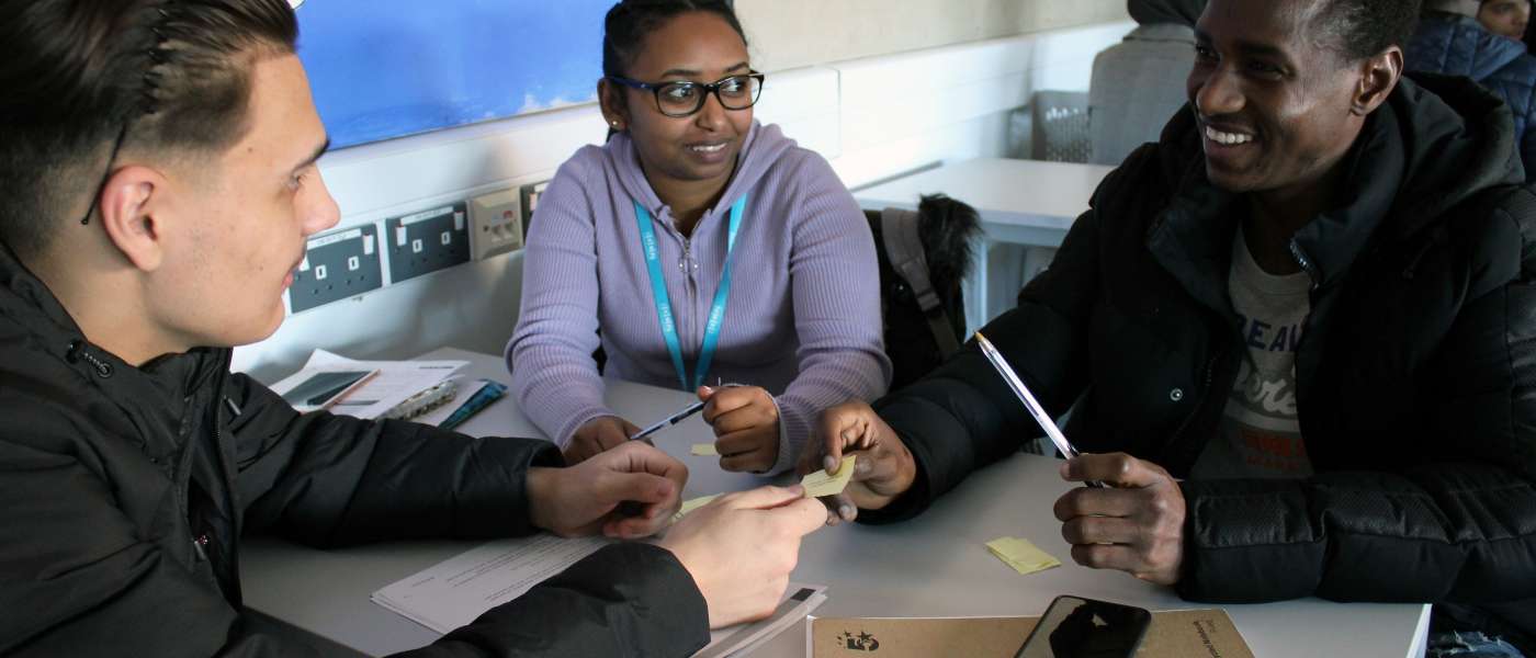 1 female and 2 male students working at desk smiling in classroom