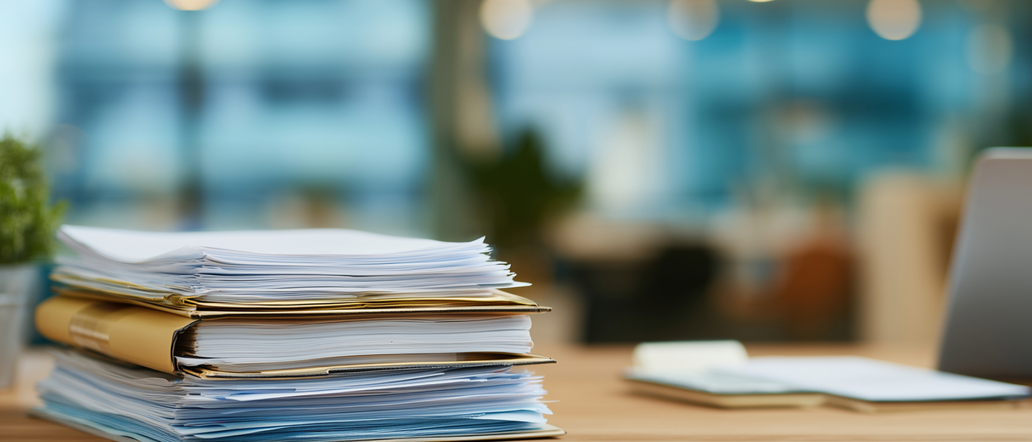 A stack of documents and folders sits on a desk in an office, representing policies, procedures and administrative records.
