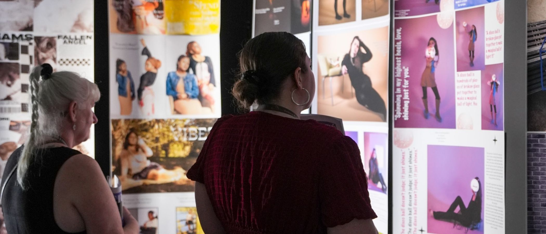 Two visitors browse creative portfolio displays in a gallery exhibition