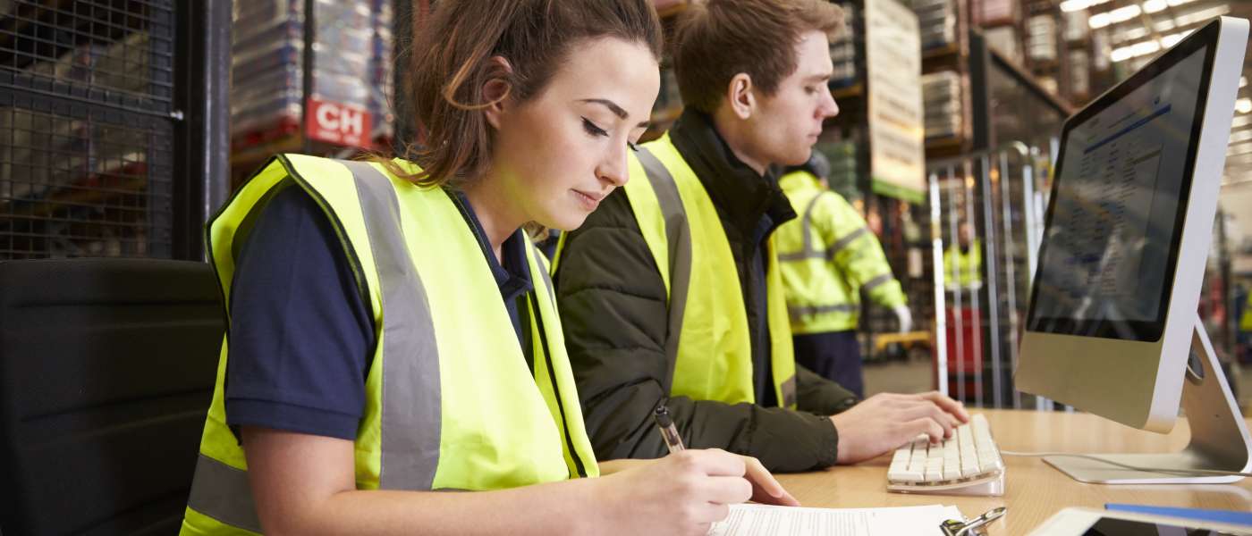 Two learners wearing hi-vis working on computer in warehouse