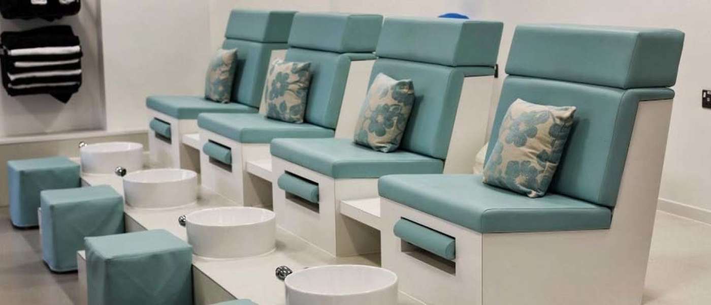 Four blue salon chairs with white and blue cushions and foot spas. Black towels on the wall next to the chairs