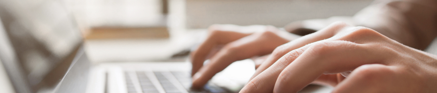 A close-up of hands typing on a laptop keyboard, with the screen and background softly blurred.