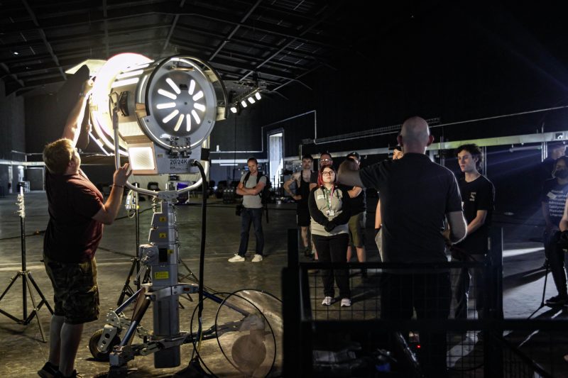 Katie Brett centre glasses watches as Toby Dare MBS Group shows students how to set up film lighting equipment