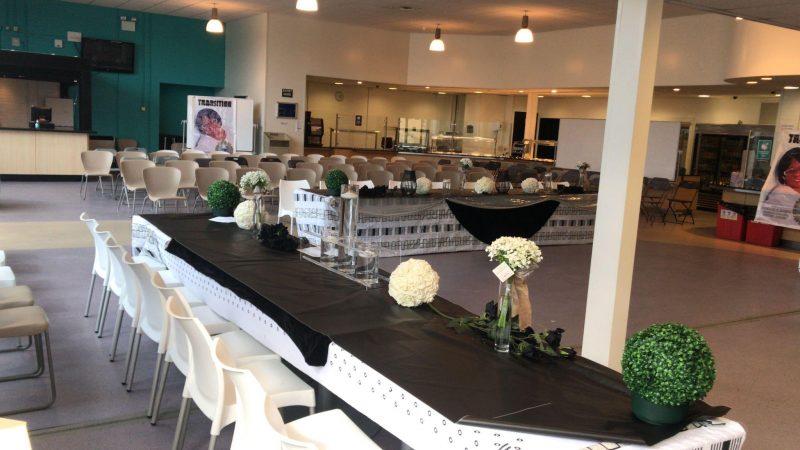 Table and chairs set up in the Refectory for an event. White chairs and black table clothes with flower bouquets across the table