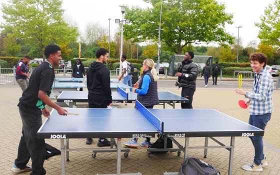Many learners outside smiling and playing table tennis. Trees in the background