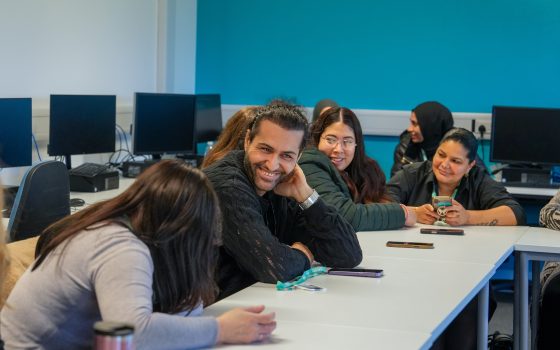 Male and female learners in classroom smiling at desk