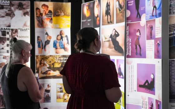 Two visitors browse creative portfolio displays in a gallery exhibition