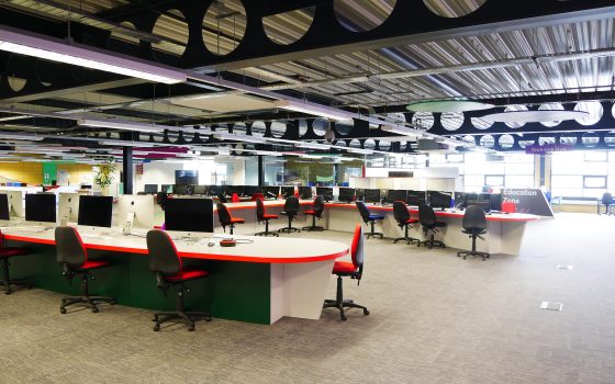 Wide view of the iCreate centre at Rush Green Campus. Long red and white tables and red tables fill the room, with iMac computers on the desks