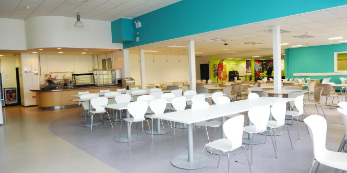 Table and chairs in the Refectory at Rush Green Campus. Food counter in the far back and student lounge far back on the right