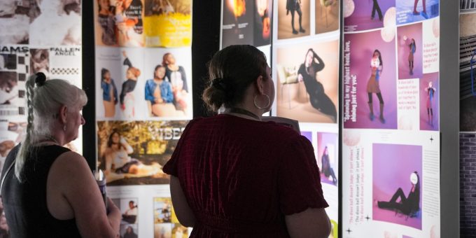 Two visitors browse creative portfolio displays in a gallery exhibition
