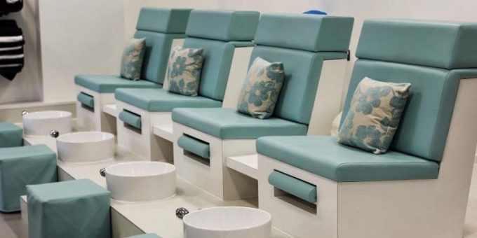 Four blue salon chairs with white and blue cushions and foot spas. Black towels on the wall next to the chairs